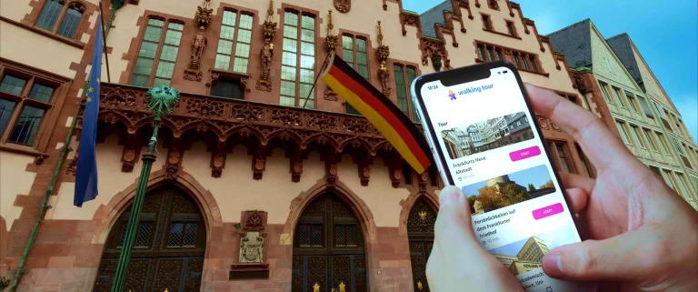 Person hält Smartphone mit Walking Tour App Tourenübersicht vor Gebäuden der Frankfurter Altstadt